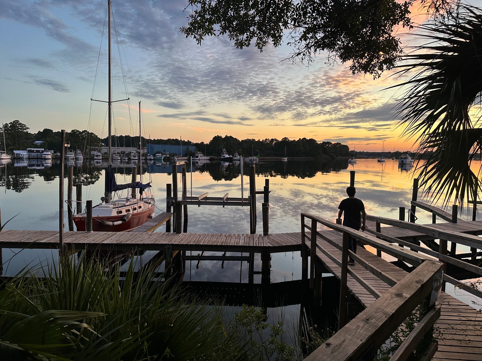 A wooden boardwalk and a docked sailboat on calm water at the Apalachicola waterfront at dusk.
